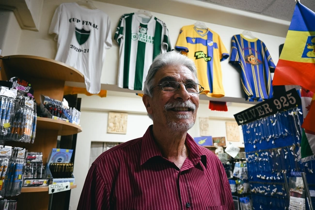 Ο κύριος Παύλος με τη συλλογή ποδοσφαιρικών φανελών στους τοίχους του καταστήματός του.