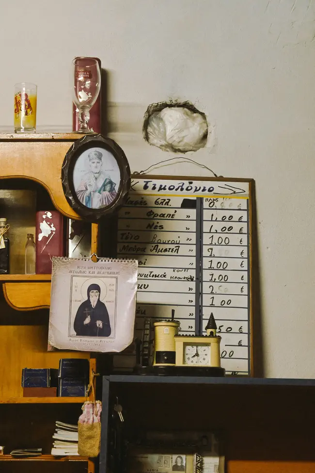 Ο τιμοκατάλογος που έχει μείνει άθικτος δίπλα στην εικόνα του Αγίου Νικολάου και το ημερολόγιο με τη μορφή του Αγίου Κοσμά του Αιτωλού.