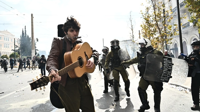 Μουσικός παίζει κιθάρα εν μέσω των επεισοδίων στο Σύνταγμα