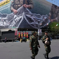 Ένστολοι περπατούν μπροστά από μια αντι-αμερικανική πινακίδα που απεικονίζει αμερικανικό αεροσκάφος να πιάνεται από ιρανικές ένοπλες δυνάμεις σε ένα δίχτυ ψαρέματος