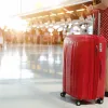 Ταξιδιώτισσα σε αεροδρόμιο με κόκκινη βαλίτσα