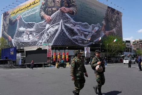 Ένστολοι περπατούν μπροστά από μια αντι-αμερικανική πινακίδα που απεικονίζει αμερικανικό αεροσκάφος να πιάνεται από ιρανικές ένοπλες δυνάμεις σε ένα δίχτυ ψαρέματος