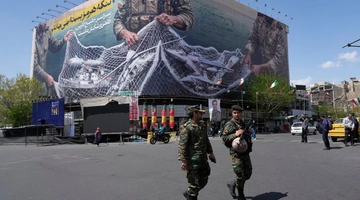 Ένστολοι περπατούν μπροστά από μια αντι-αμερικανική πινακίδα που απεικονίζει αμερικανικό αεροσκάφος να πιάνεται από ιρανικές ένοπλες δυνάμεις σε ένα δίχτυ ψαρέματος