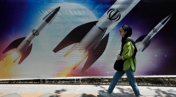 Μια γυναίκα περνάει δίπλα από ένα πανό που δείχνει πυραύλους να εκτοξεύονται, στη βόρεια Τεχεράνη 